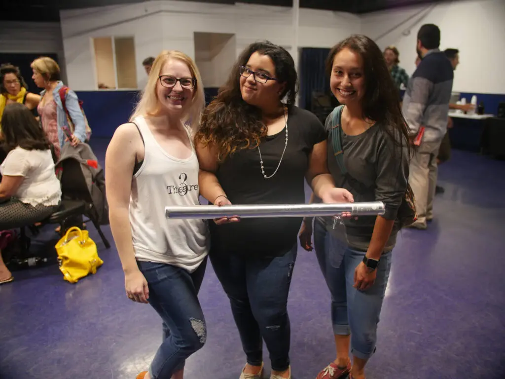 Three actors hold a random prop