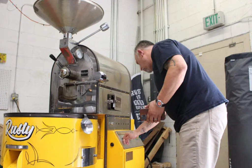 A man leans over a custom-painted industrial coffee grinder.