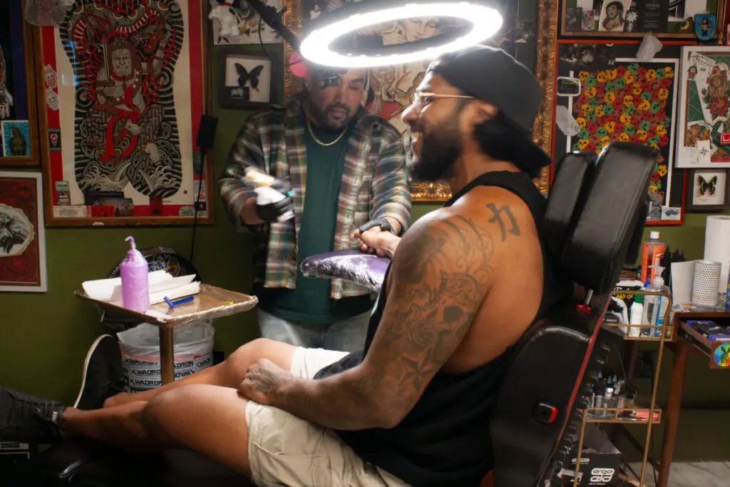 A bearded man sits in a tattoo shop chair.