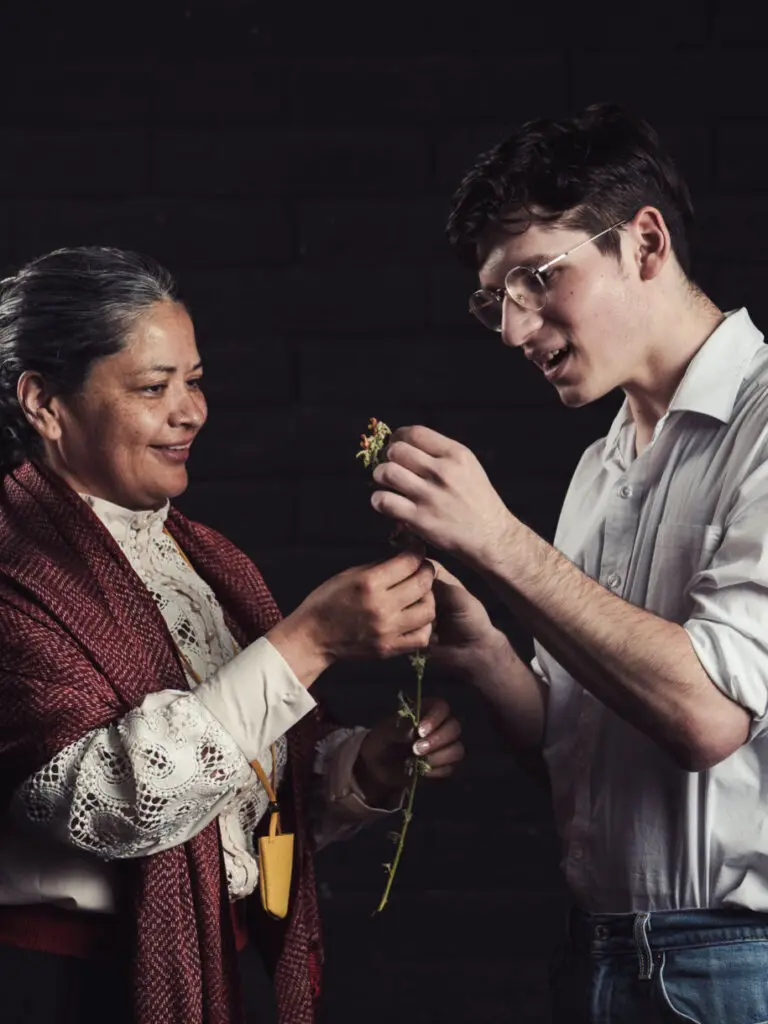A young man stands next to an older woman holding some herbs.