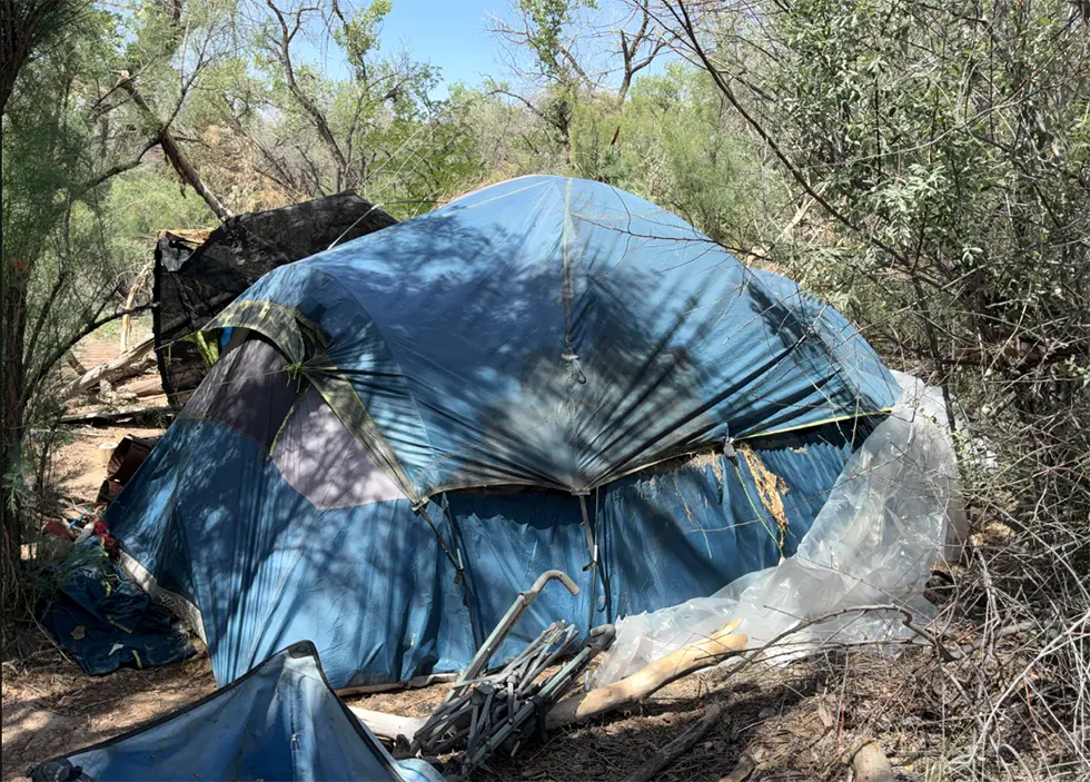 A blue dome tent stands in the Bosque, surrounded by plastic sheeting and personal belongings. (Courtesy Bernalillo County)