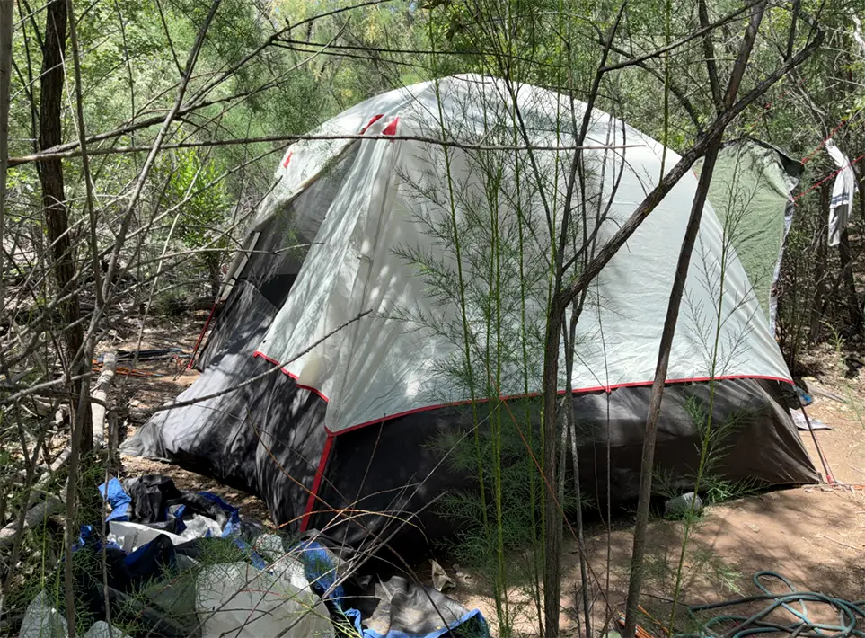 A gray-and-white tent stands in the Bosque, with clothing and personal belongings scattered along its side. (Courtesy Bernalillo County)