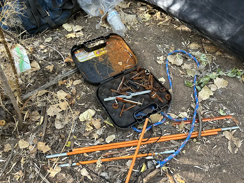 An open case containing a syringe and rusted hardware sits among rope and tent poles left behind at a Bosque encampment. (Courtesy Bernalillo County)