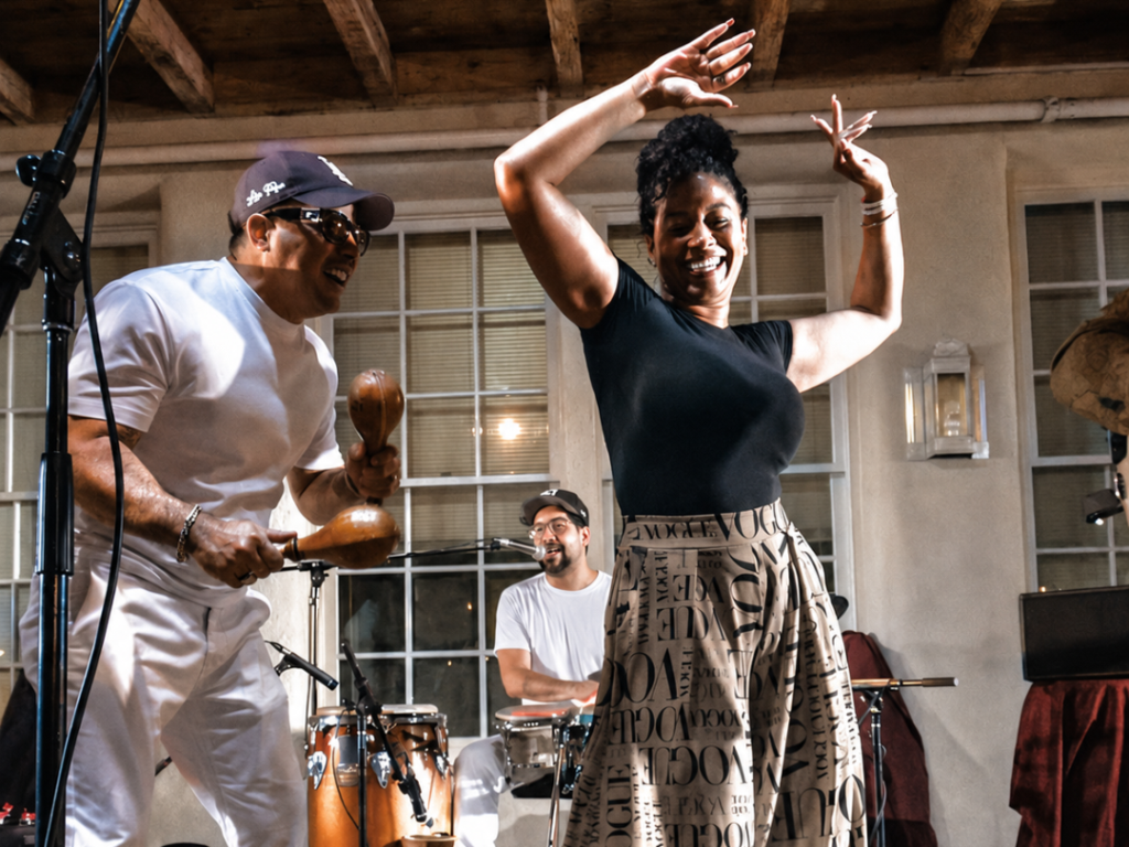 A woman dances a Latin dance while two percussionists perform behind her.