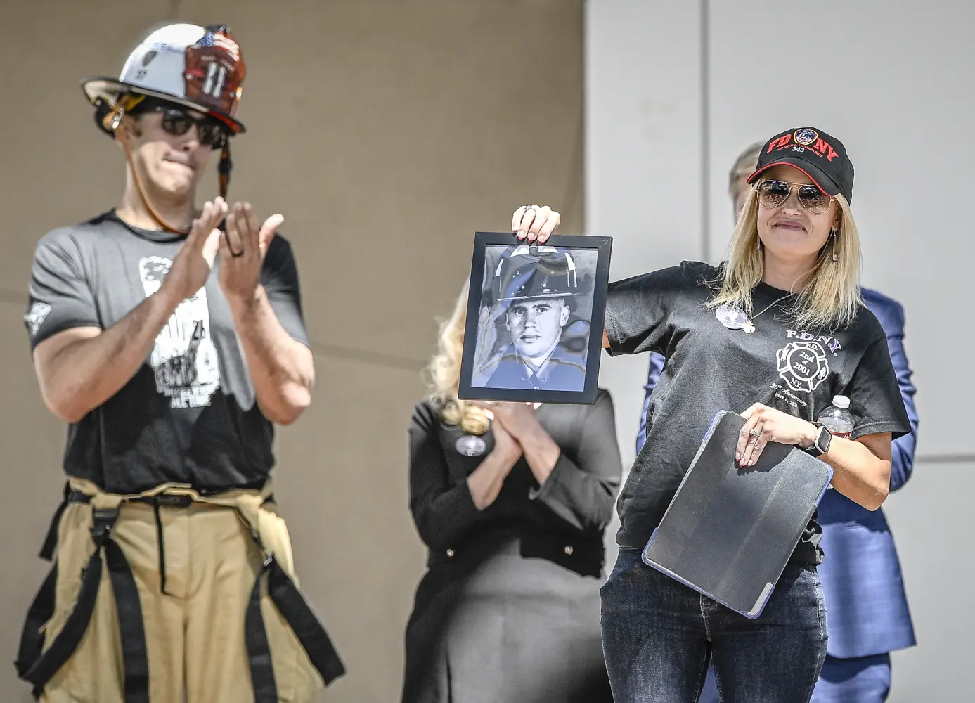 A Woman hold up a photo of a fallen fire fighter at a 9/11 Memorial.