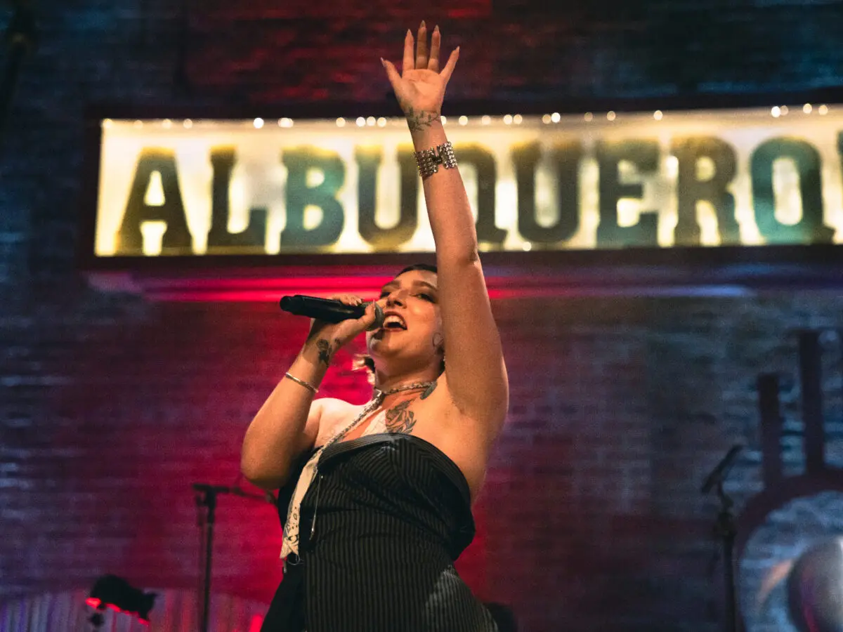 A singer stands on stage with a microphone, her arm raised.