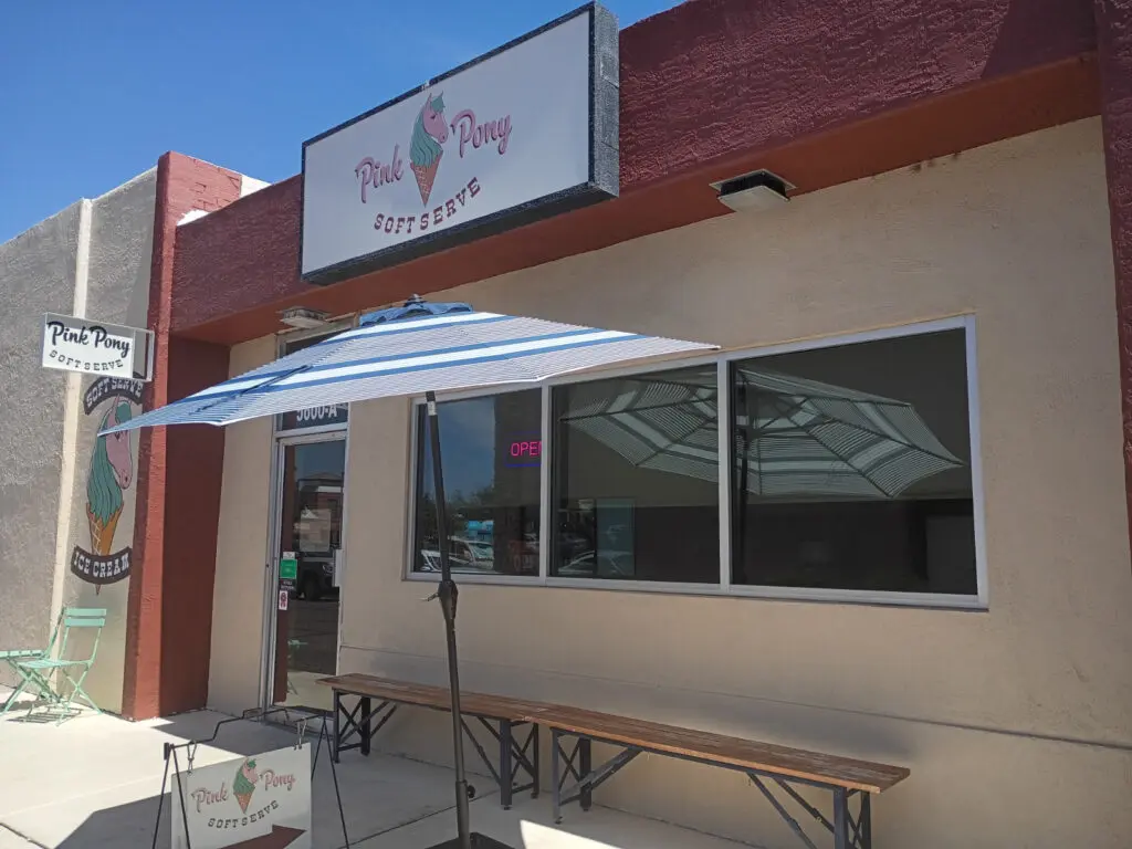 The outside window of an ice cream parlor with an umbrella out front.
