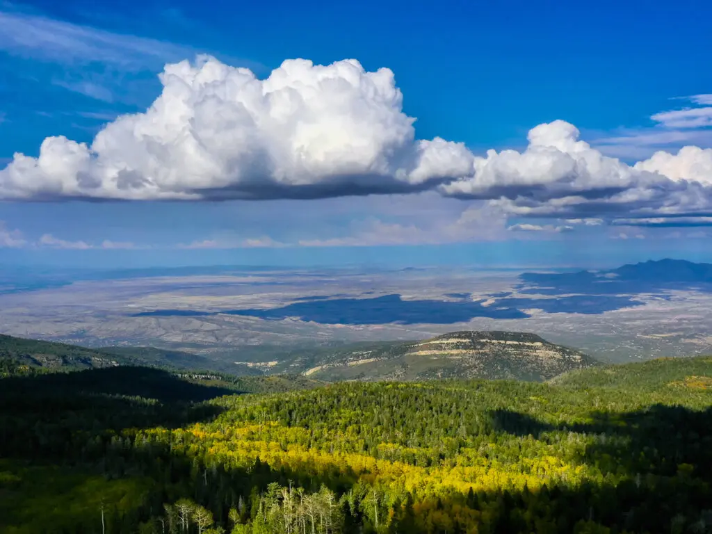 Clouds drift over the mountains which are covered in fall colors.