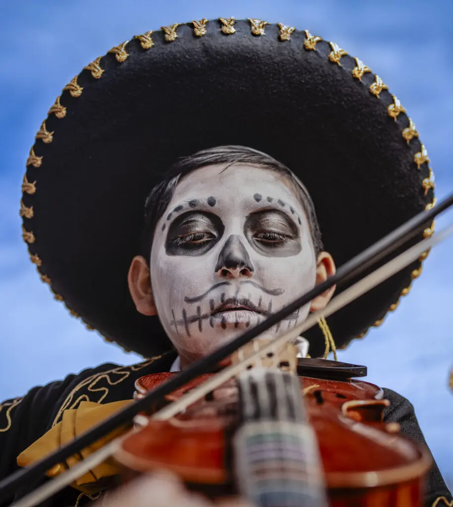 A child playing the violin at the Muertos y Marigolds parade. (Photo by Roberto Rosales) 