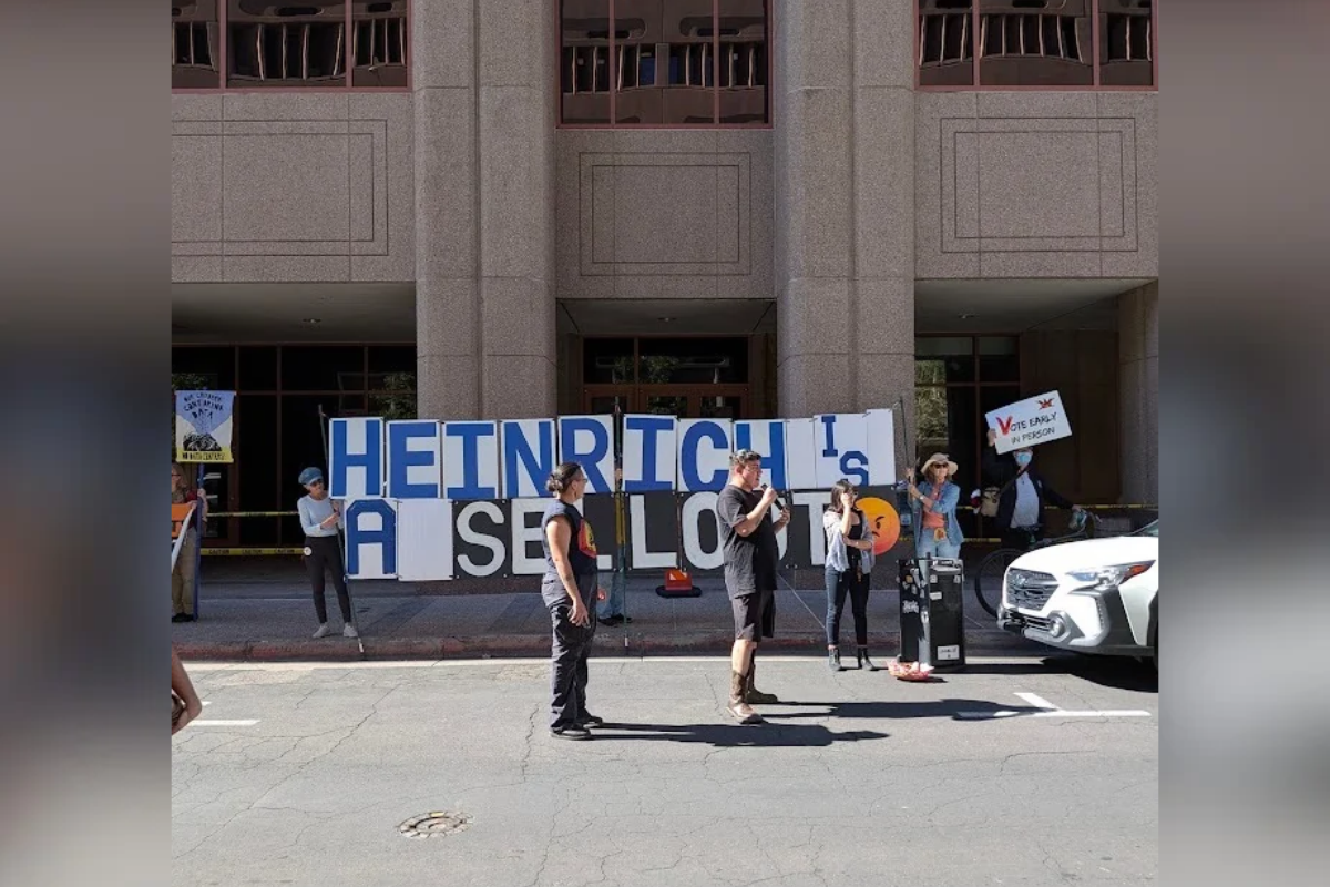 A speaker addresses the crowd in front of a sign reading “Heinrich is a sellout” during a rally outside U.S. Sen. Martin Heinrich’s downtown Albuquerque office Tuesday, Oct. 27, 2026. Students and community members marched from the University of New Mexico to protest AI data centers and the Heinrich-backed Bipartisan American Affordability and Jobs Act. (Kevin Hendricks/The Paper)