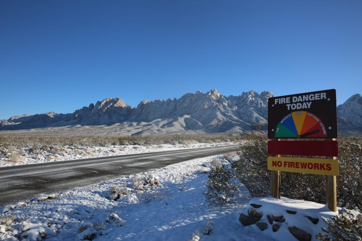 A fire danger sign amidst the rare snows on Chihuahua desert landscape leading up to the Organ mountains, captured on Jan. 10, 2025. (Danielle Prokop / Source NM)