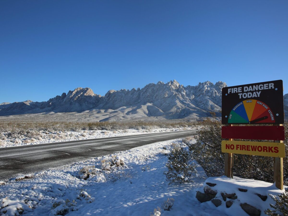 A fire danger sign amidst the rare snows on Chihuahua desert landscape leading up to the Organ mountains, captured on Jan. 10, 2025. (Danielle Prokop / Source NM)