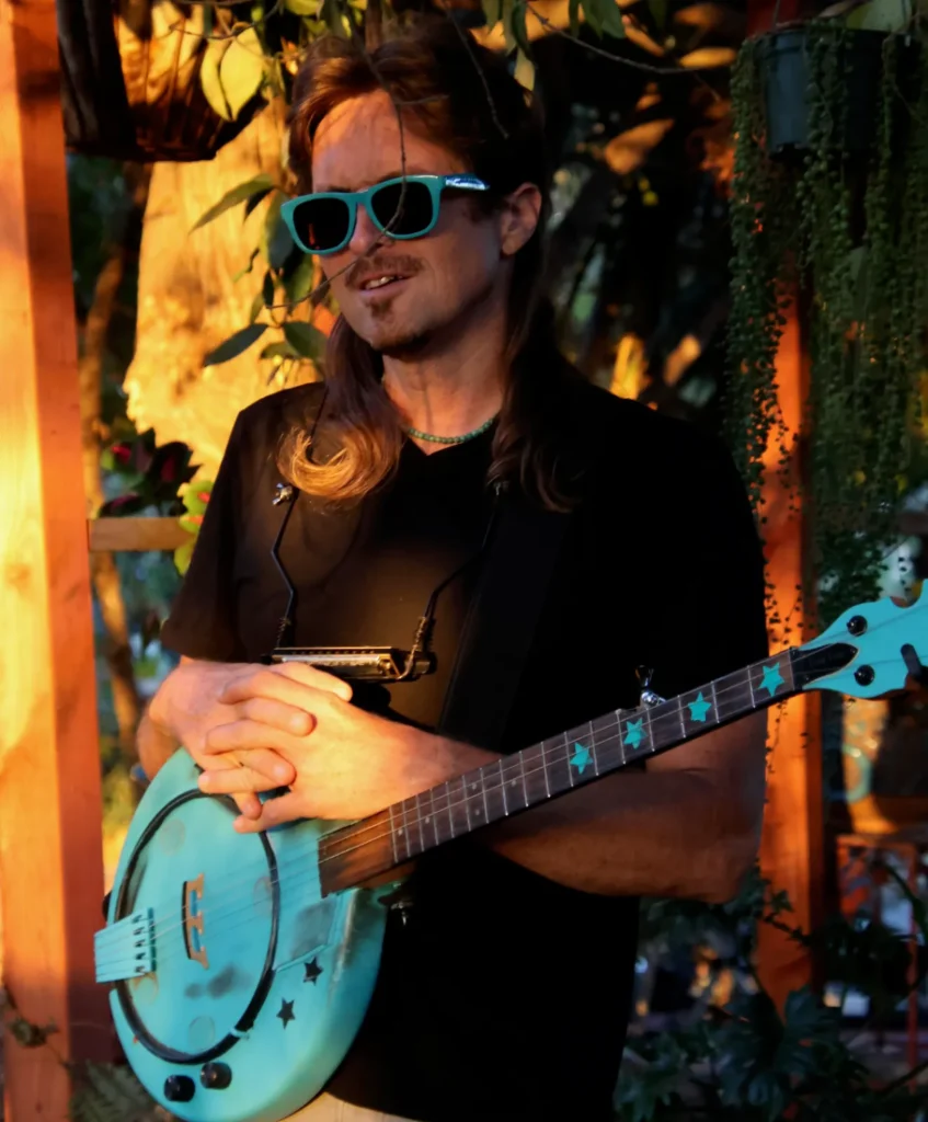 A man in sunglasses holds a guitar