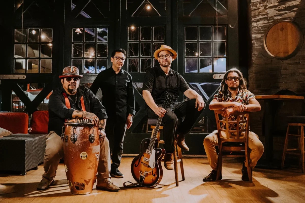 Four members of a band pose on stage with their instruments.