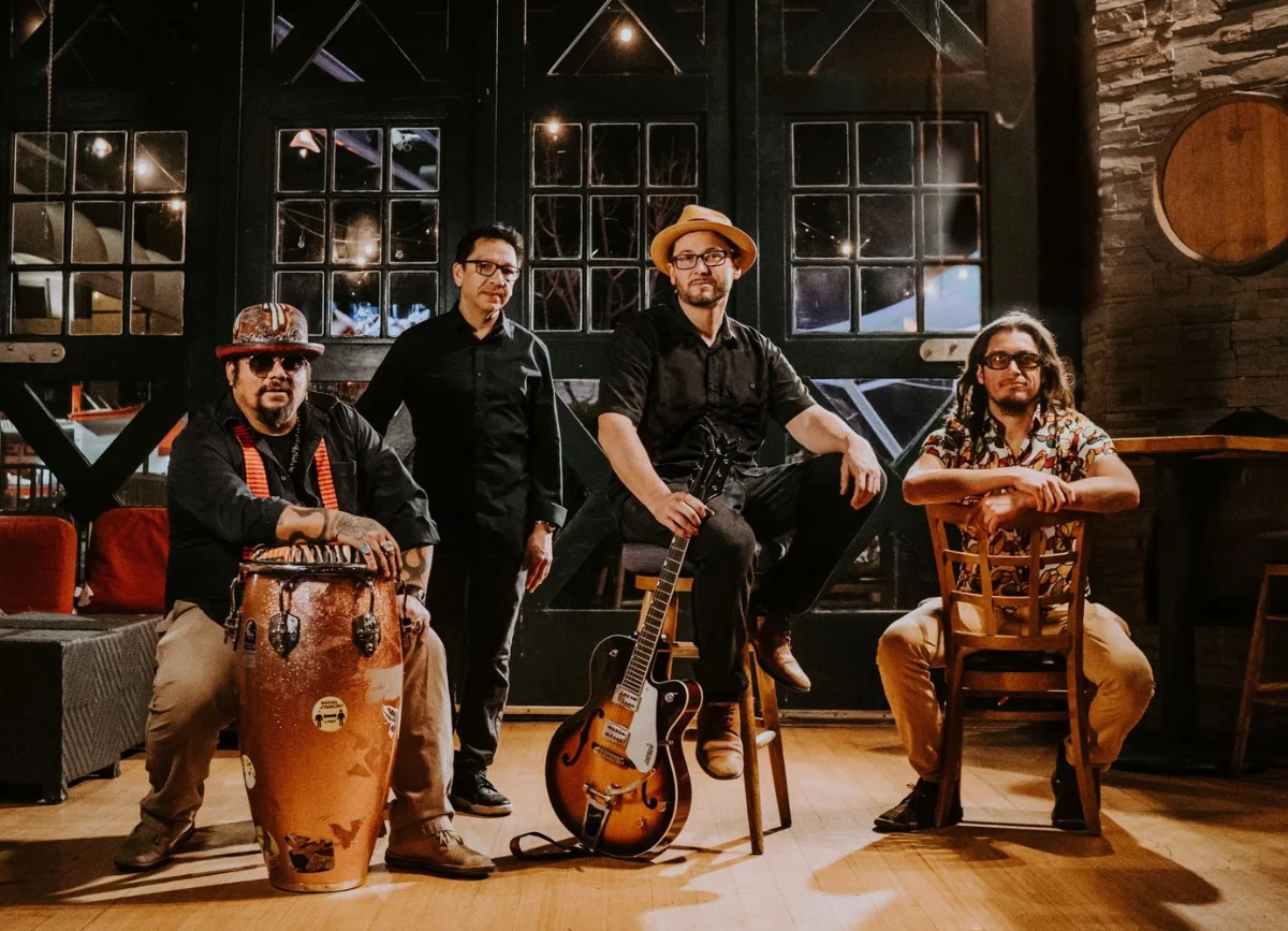 Four members of a band pose on stage with their instruments.