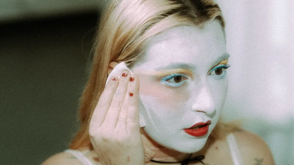 A blonde woman applies heavy pancake makeup to her face.
