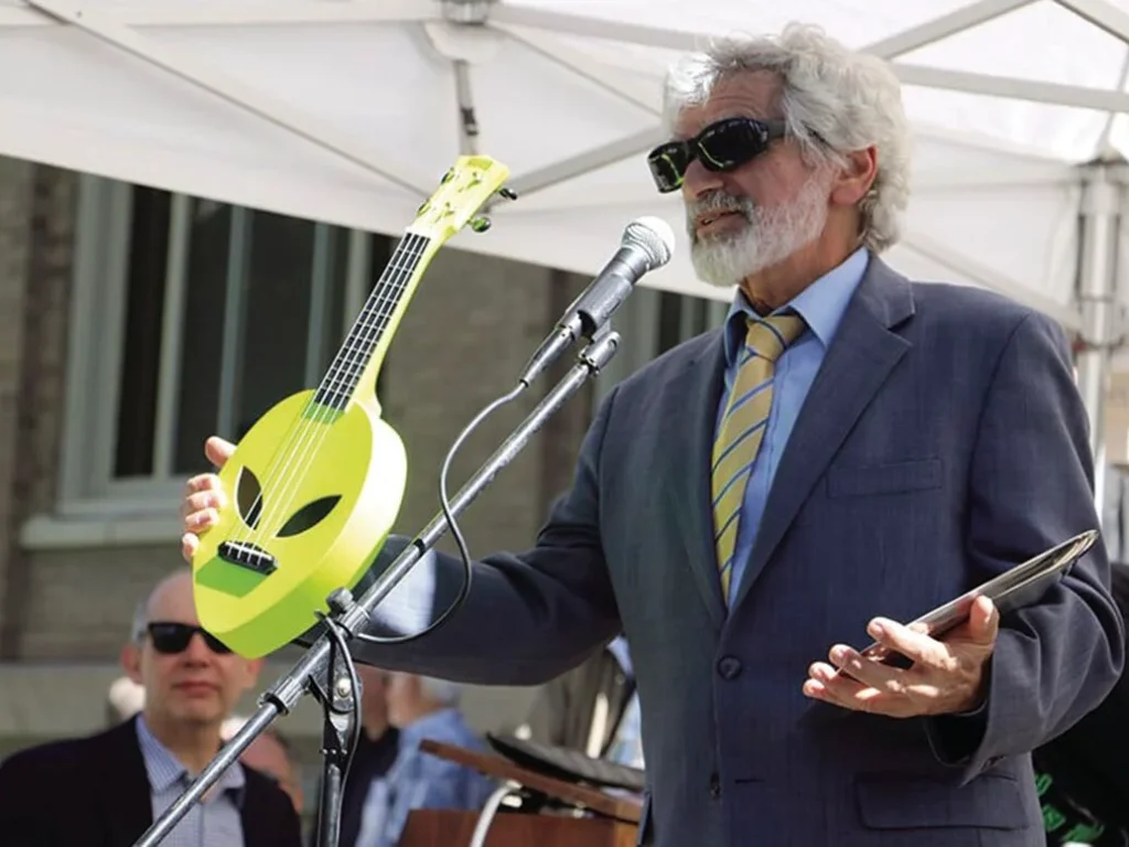 A musician holds a guitar in the shape of a alien head.